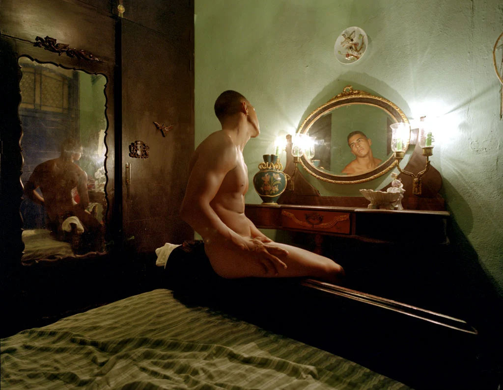 An intimate interior: a seated man faces a mirror in a warmly lit room.